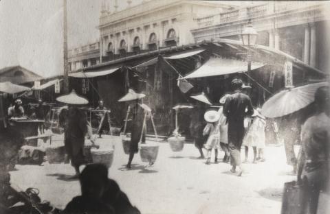 Porters carrying baskets, by a street market outside Queen's College, Hollywood Road
