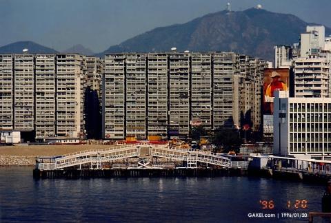 1996 HK harbor: Ferry Point Estate blocks behind a floating pier bridge, with mountains in back.