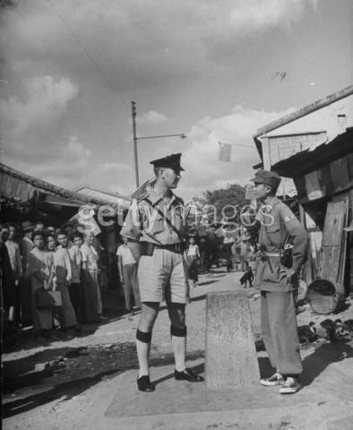 British police inspector (L) standing on his half of the village while Red Chinese Army irregular standing on the right side of the border marker which divides the village. 1949 10 1