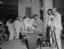 Major-General Okada signs the Instrument of Surrender while Vice Admiral Fujita awaits his turn, Government House